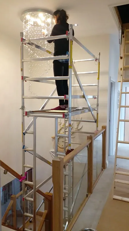 Electrician using a dedicated stair access tower to reach a high ceiling light fixture